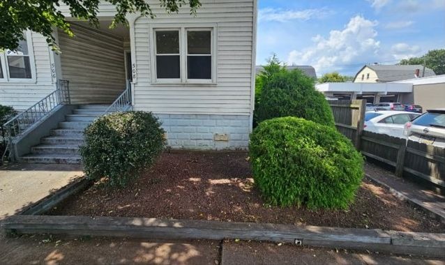 Fresh dark mulch raked around three reshaped shrubs, with the entry steps cleared and the bed edged
