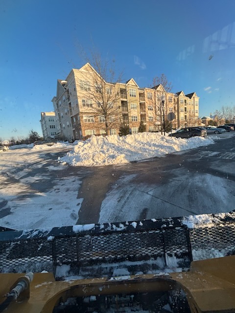 From inside the plow truck: a commercial parking lot cleared, snow pushed into long banks in front of an apartment building